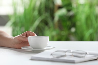 Photo of Woman holding cup of coffee at white table indoors, closeup