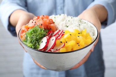 Woman holding delicious poke bowl with salmon and vegetables, closeup
