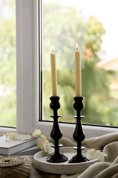 Photo of Pair of beautiful black candlesticks, books and round wicker box on windowsill