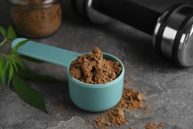 Hemp protein powder, fresh leaves and dumbbell on grey table, closeup