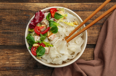 Tasty cooked rice noodles with chicken and vegetables on wooden table, top view