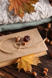 Photo of Book with autumn leaf as bookmark, acorns and warm sweaters on wooden table