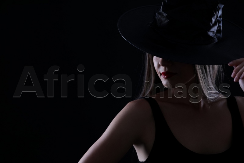 Young woman wearing witch costume on black background, space for text. Halloween party