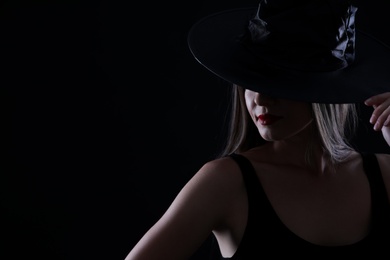 Young woman wearing witch costume on black background, space for text. Halloween party