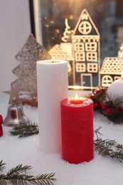 Beautiful burning candles with Christmas decor near window
