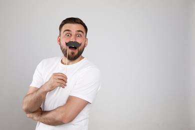 Photo of Emotional man with fake mustache on light grey background, space for text