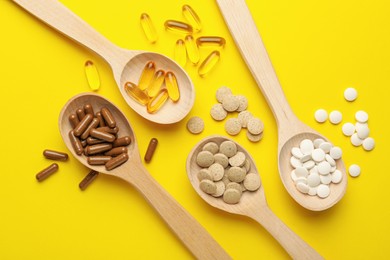 Wooden spoons and different dietary supplements on yellow background, flat lay