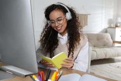 African American woman with headphones using modern computer for studying at home. Distance learning