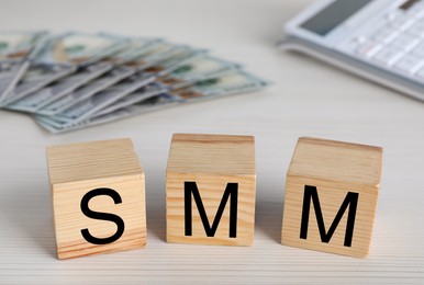 Cubes with abbreviation SMM (Social media marketing), money and calculator on white wooden table