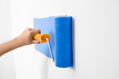 Woman painting white wall with blue dye, closeup. Interior renovation