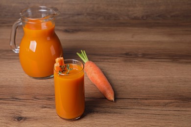 Carrot juice in glass and jug on wooden table