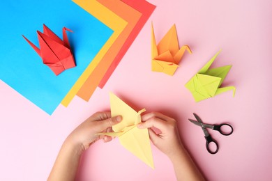 Photo of Origami art. Child holding paper figure on pink background, closeup and top view