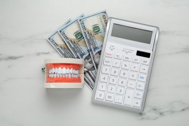 Educational dental typodont model, dollar banknotes and calculator on white table, flat lay. Expensive treatment