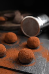 Delicious chocolate truffles powdered with cocoa on black table, closeup