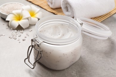 Body scrub, towels and plumeria flowers on grey table, closeup