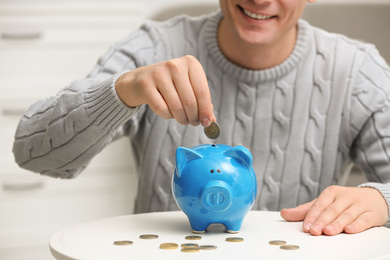 Man putting coin into piggy bank at white table, closeup