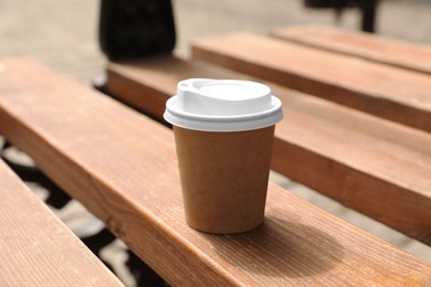 Takeaway paper cup with hot coffee on wooden bench outdoors