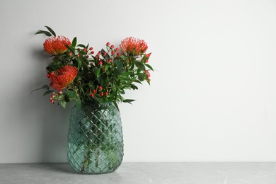 Photo of Bouquet with beautiful red protea flowers in glass vase on grey table against white background. Space for text