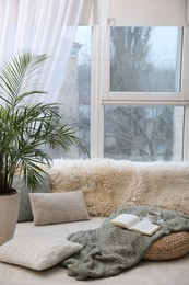 Comfortable lounge area with faux fur and pillows near window in room