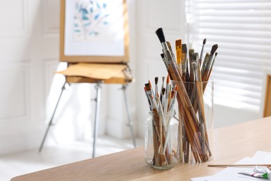 Holders with different paintbrushes on wooden table in studio, space for text. Artist's workplace