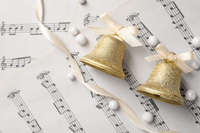 Photo of Golden shiny bells with white bows on music sheets, flat lay and space for text. Christmas decoration