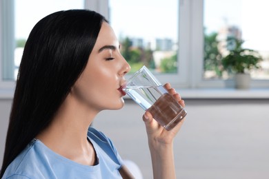 Photo of Young beautiful woman drinking water indoors. Refreshing drink