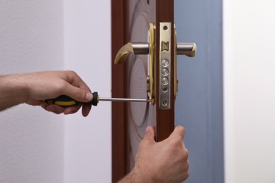 Handyman with screwdriver repairing door lock, closeup