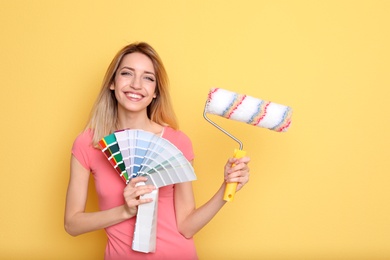 Young woman with color palette and roller on yellow background
