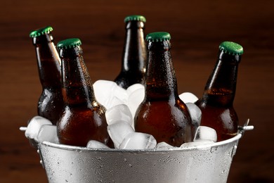 Photo of Metal bucket with bottles of beer and ice cubes on wooden background, closeup