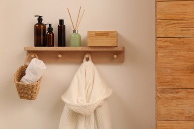 Wooden shelf with toiletries, fresh towel and bathrobe on beige wall. Interior element