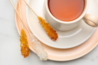 Photo of Sticks with sugar crystals served to tea on white marble table, top view