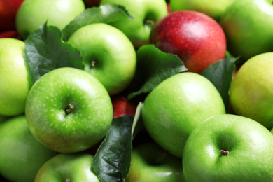 Pile of tasty ripe apples with leaves as background, closeup