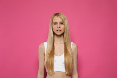 Beautiful young woman with long straight hair on pink background