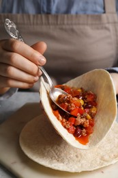 Woman putting tasty chili con carne into tortilla at white table, closeup