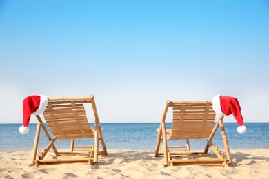 Photo of Sun loungers with Santa's hats on beach, space for text. Christmas vacation