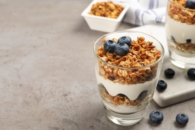 Photo of Glasses of yogurt with granola and blueberries on grey table, closeup. Space for text