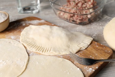 Photo of Raw chebureki with tasty filling and fork on wooden table, closeup