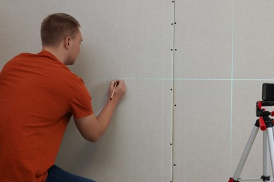Man using cross line laser level and pencil for accurate measurement on plasterboard, back view