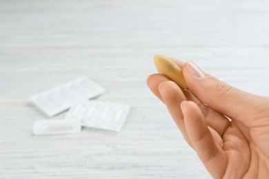 Woman holding suppository at white wooden table, closeup. Hemorrhoid treatment