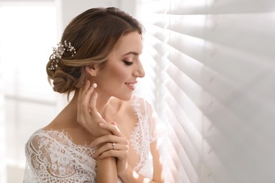 Young bride with elegant wedding hairstyle near window indoors