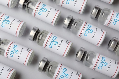Glass vials with COVID-19 vaccine on light background, flat lay