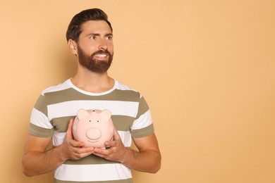 Photo of Happy man with ceramic piggy bank on beige background, space for text