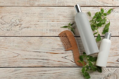 Stinging nettle, cosmetic products and comb on white wooden background, flat lay with space for text. Natural hair care