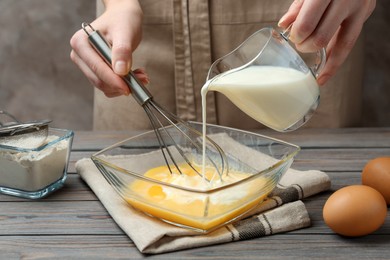 Woman adding milk to whisked eggs at wooden table, closeup