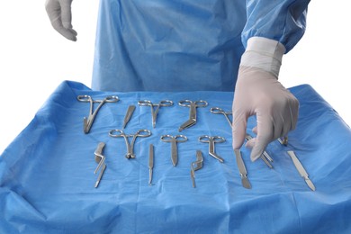 Doctor near table with surgical instruments on light background, closeup