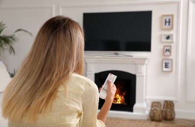 Young woman watching television at home, back view. Living room interior with TV on fireplace