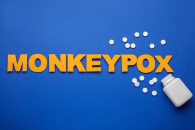 Word Monkeypox, bottle and pills on blue background, flat lay