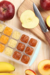 Photo of Different purees in ice cube tray and different fresh fruits on wooden table, flat lay. Ready for freezing