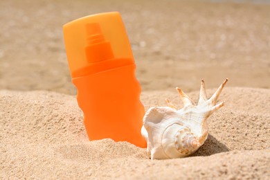 Photo of Bottle with sun protection spray and seashell on sandy beach, closeup