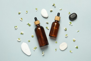 Flat lay composition with bottles of face serum, spa stones and beautiful flowers on light grey background
